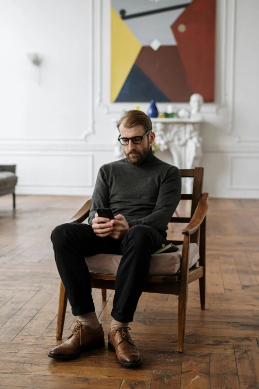 a man sitting in a chair looking at his cell phone, inspired by Constantin Hansen, trending on pexels, visual art, wearing turtleneck, ginger bearded man with glasses, full body in frame, sitting across the room