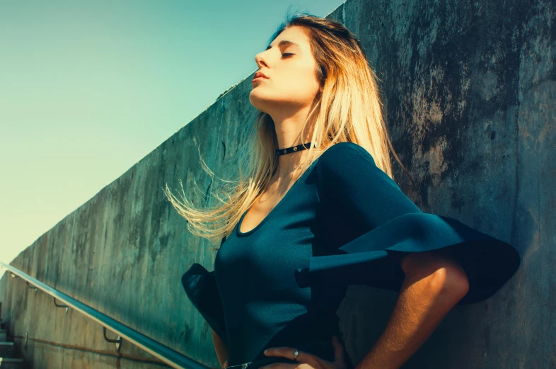 a woman leaning against a wall with her hands on her hips, pexels contest winner, aestheticism, blue toned, sunny sky, beautiful blonde woman, profile image