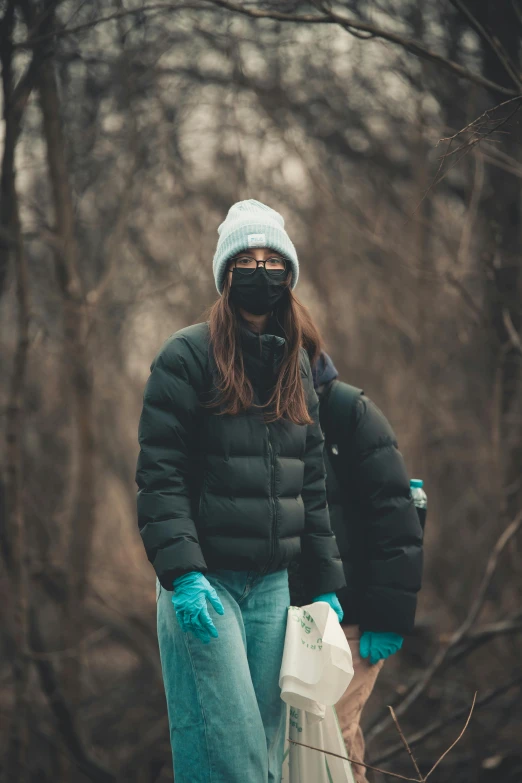 a woman in a black jacket and blue gloves, by Adam Marczyński, pexels contest winner, carrying survival gear, people are wearing masks, nature outside, trash