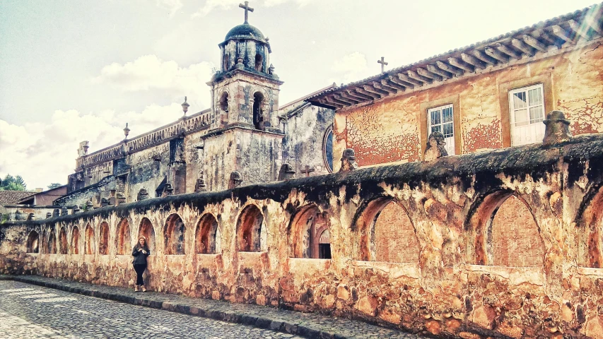 a person standing in front of a brick building, by Miroslava Sviridova, instagram, romanesque, 1 8 th century south america, st cirq lapopie, cathedral!!!!!, city wall