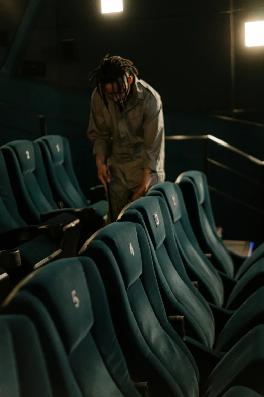 a man standing next to a row of blue chairs, playboi carti, sitting in a movie theater, making of, [ theatrical ]