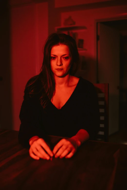 a woman sitting at a table in a dark room, red mood in background, kailee mandel, brett amory, portrait image