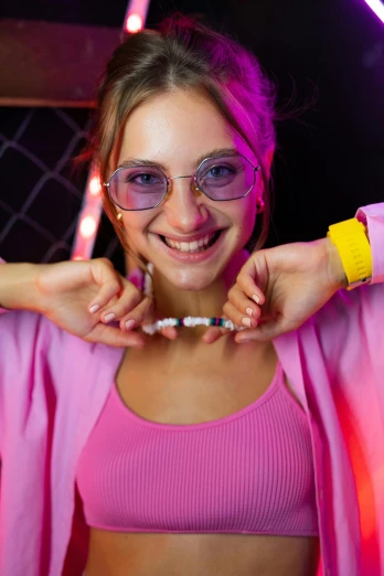 a woman in a pink top posing for a picture, by Adam Marczyński, trending on pexels, antipodeans, glow sticks, bracelets, with glasses, college party