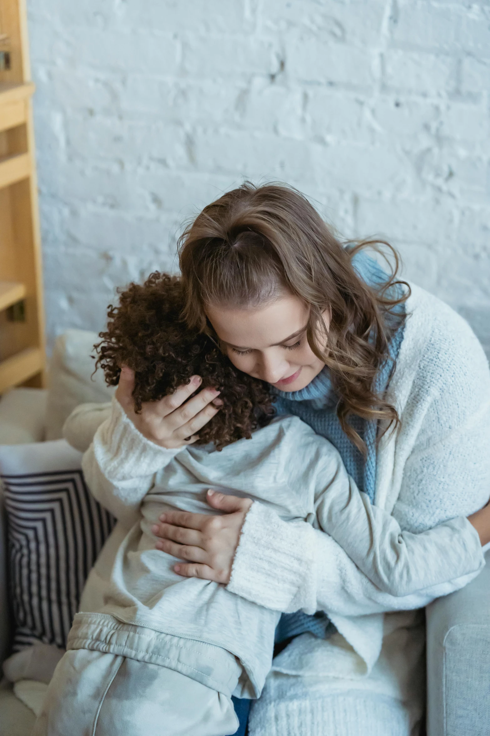 a woman sitting on a couch hugging a small child, trending on pexels, portrait of depressed teen, brown curly hair, grieving, supportive