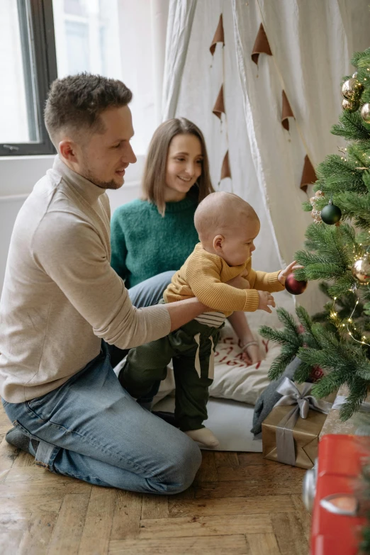 a man and woman playing with a baby near a christmas tree, pexels contest winner, folk art, apartment, square, gif, hgtv