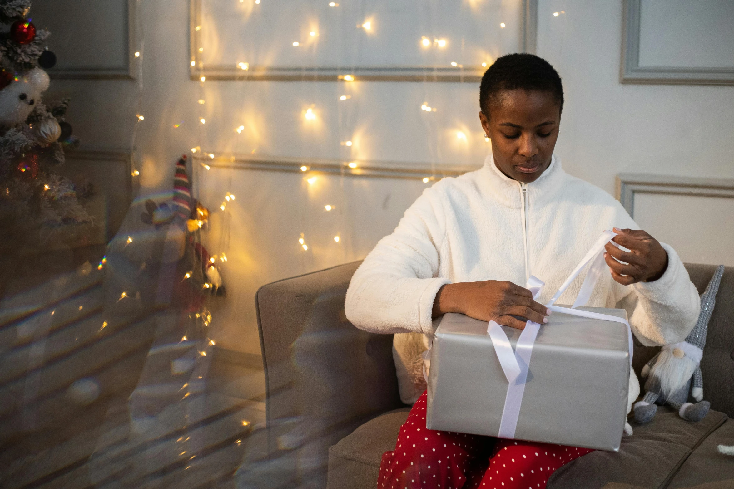 a woman sitting on a couch holding a present, by Alice Mason, pexels contest winner, black teenage boy, lights inside, white ribbon, grey