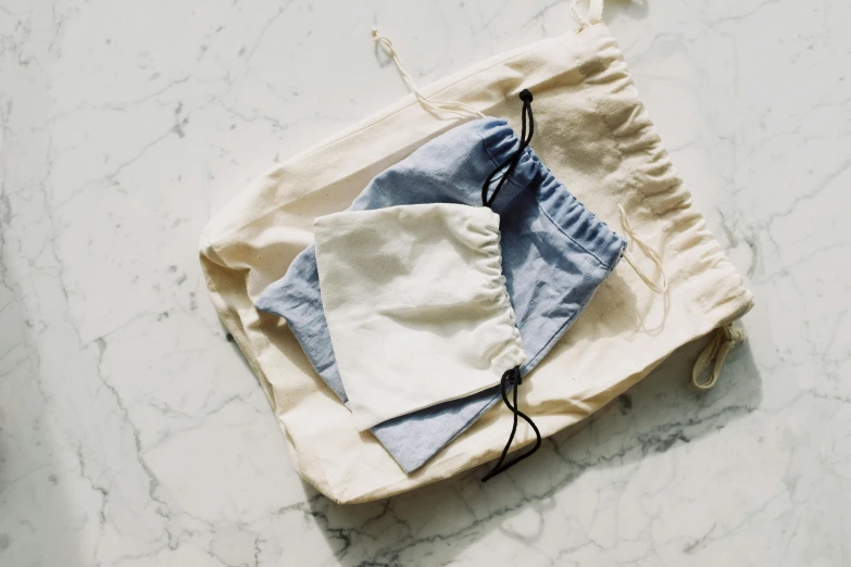 a bag sitting on top of a table next to a pair of scissors, by Nina Hamnett, unsplash, minimalism, wearing a light blue shirt, wearing white pajamas, while marble, various sizes