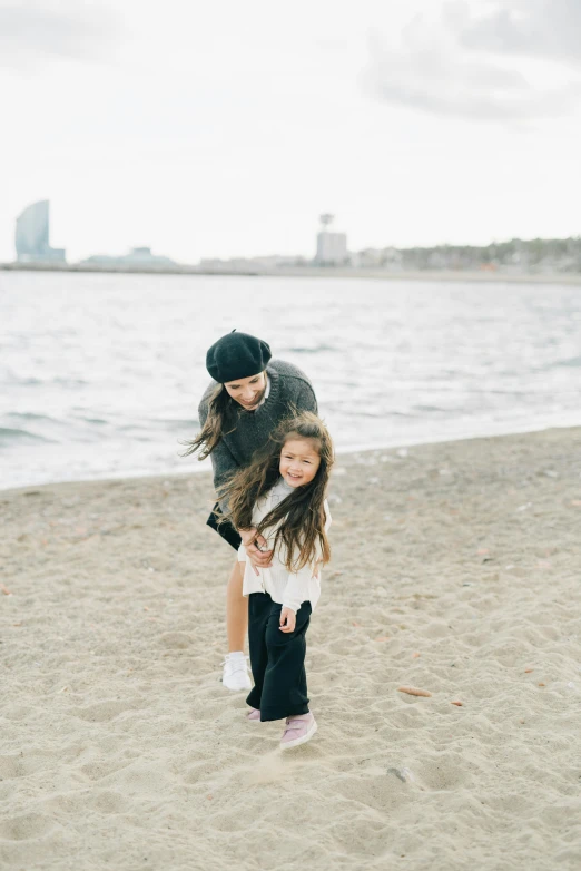 a man standing next to a little girl on a beach, by Modest Urgell, unsplash, black haired girl wearing hoodie, in barcelona, lulu chen, standing on two legs