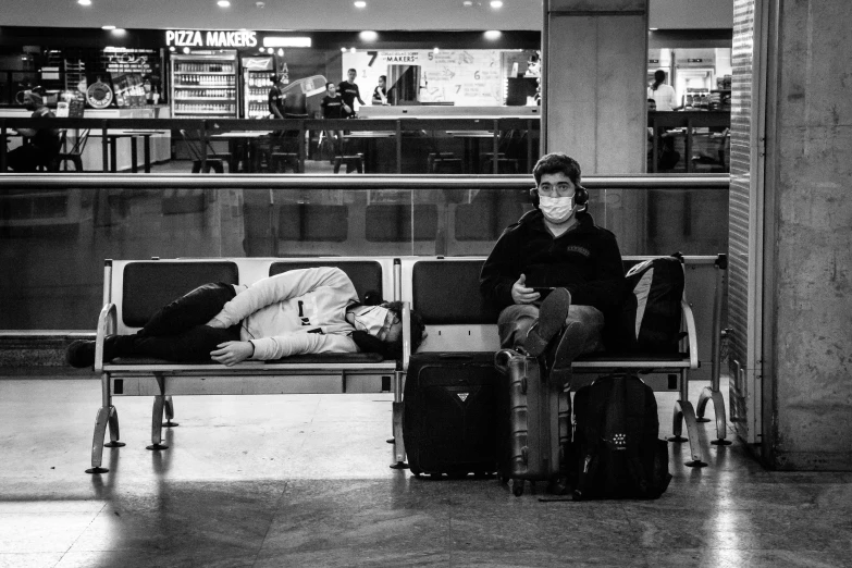 a black and white photo of a person sitting on a bench, black. airports, two people, lying on an empty, life after the plague