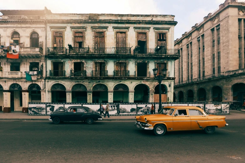 a yellow car driving down a street next to tall buildings, a photo, pexels contest winner, neoclassicism, cuban setting, an abandoned old, with an intricate, an ancient