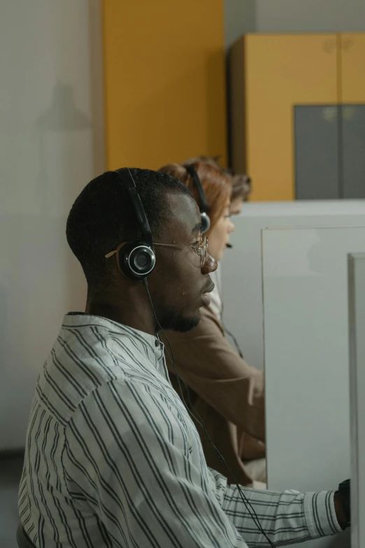 a man wearing headphones sitting in front of a computer, two people, diversity, ignant, ( ( theatrical ) )