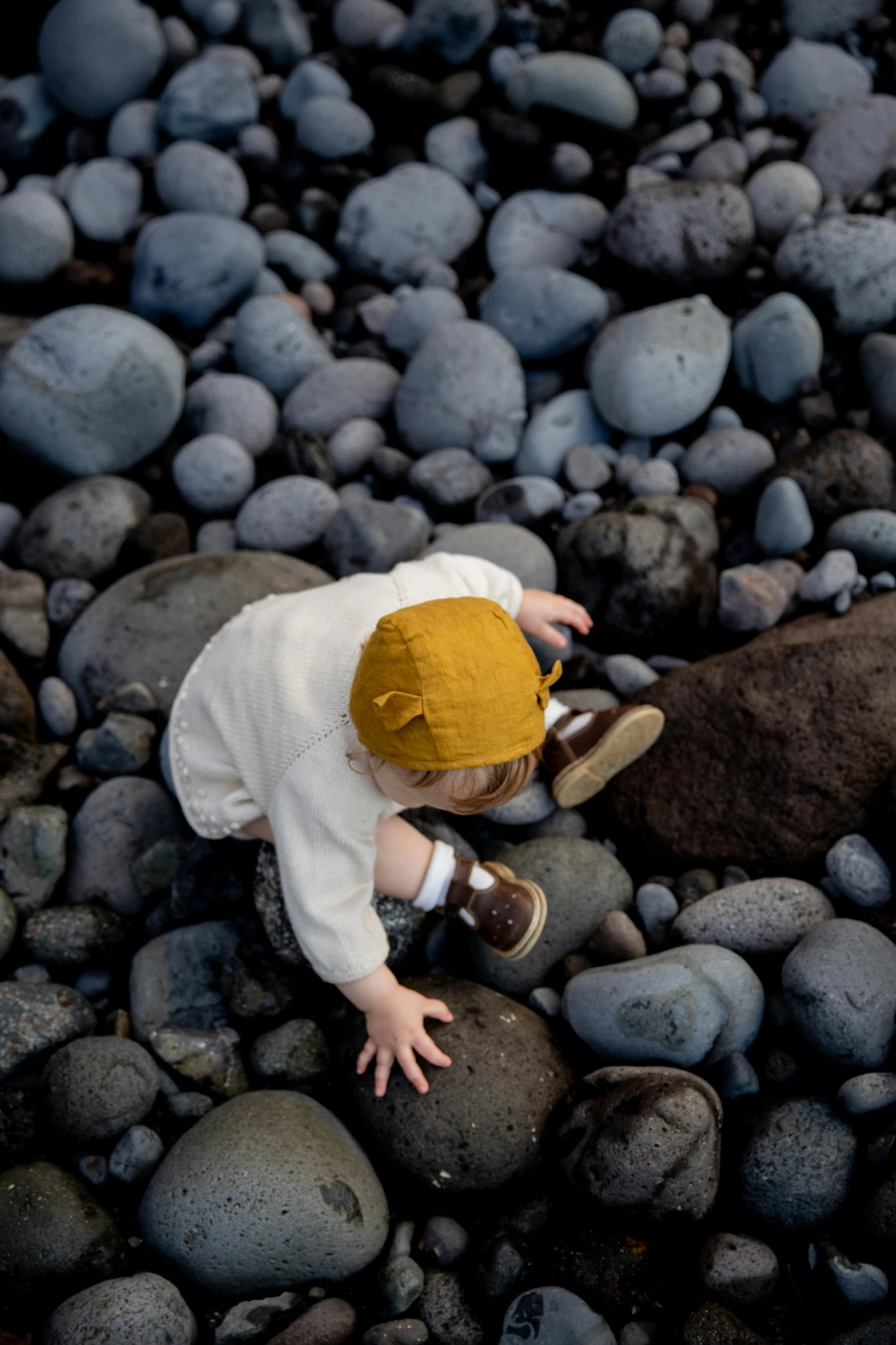 a baby laying on top of a pile of rocks, unsplash, walking on the beach, lava rock, ochre, white