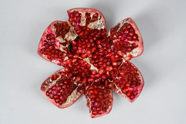 a pomegranate cut in half on a white surface, by Jan Kupecký, pexels, hurufiyya, made of flowers and berries, hexagonal shaped, judy chicago, bottom view