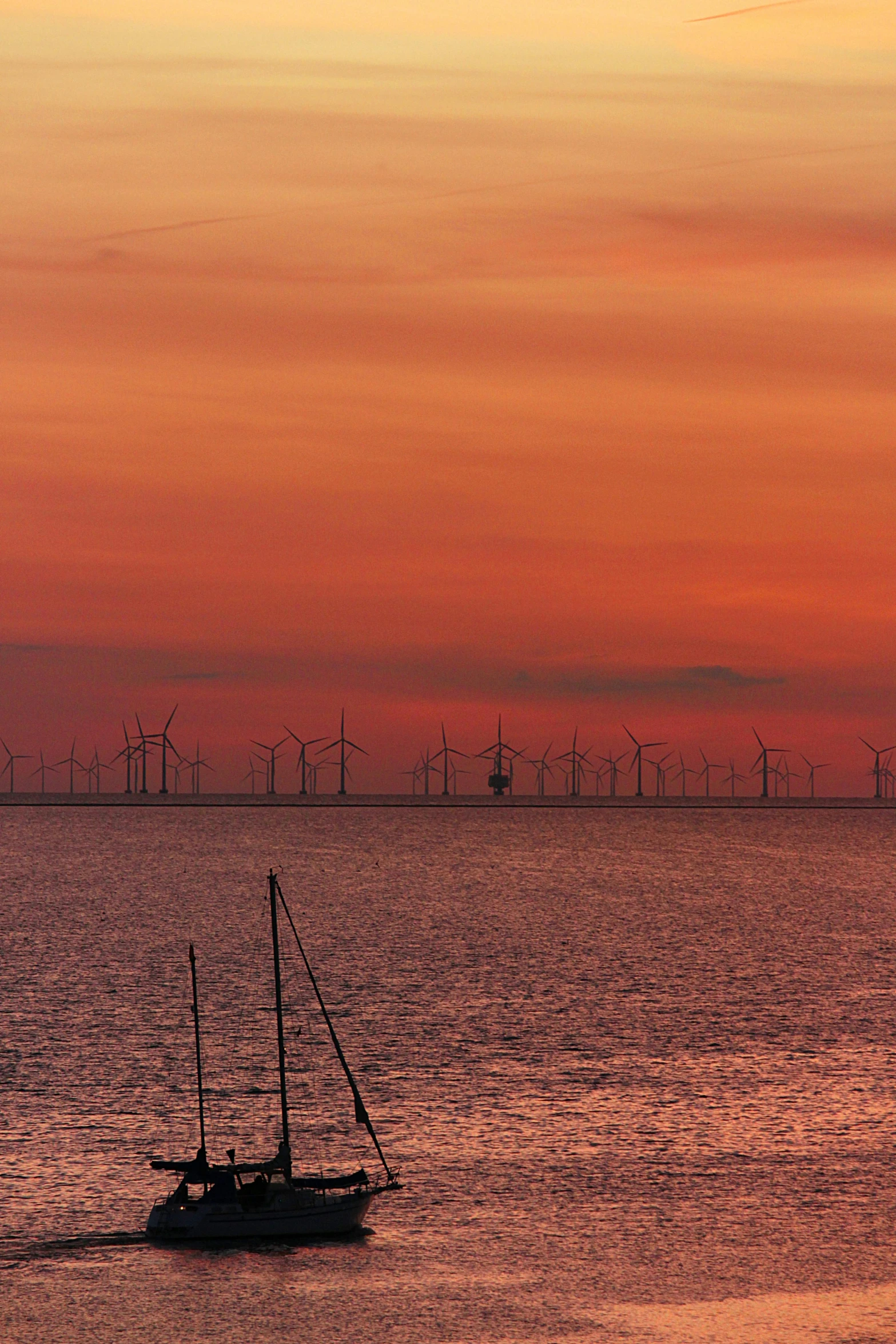 a boat floating on top of a large body of water, windmills, red skies, viewed from a distance, pylons