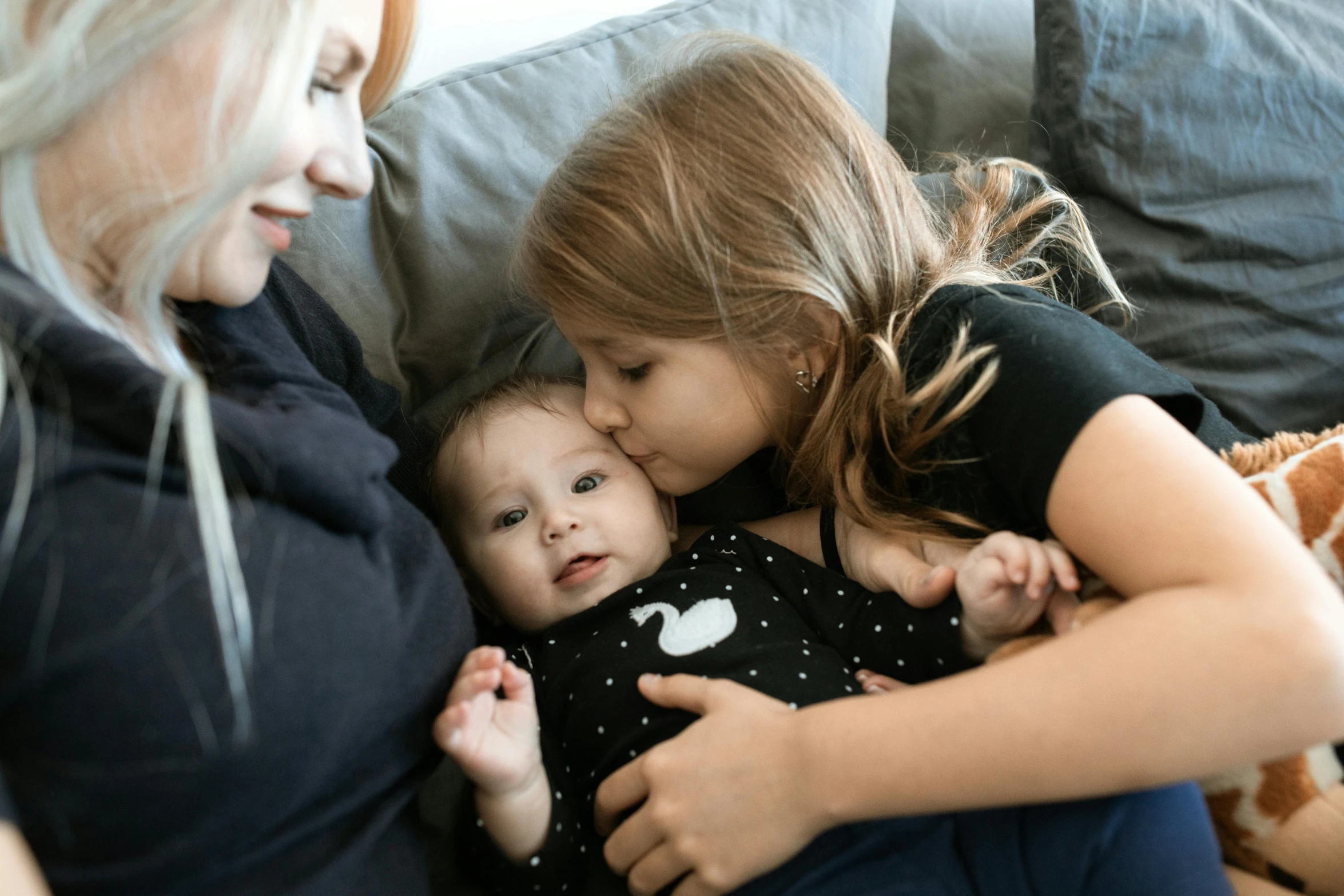 a woman sitting on top of a couch holding a baby, pexels contest winner, portrait of two girls kissing, avatar image, little brother, lesbian