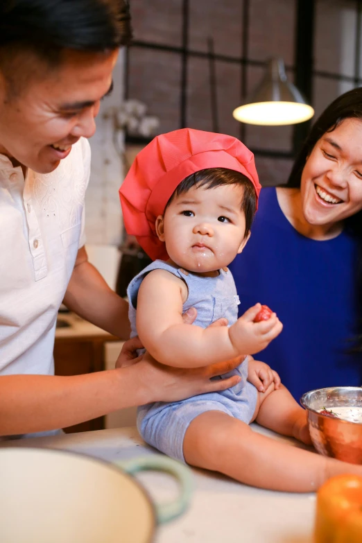 a man and woman holding a baby in a kitchen, pexels contest winner, asian descent, frosting on head and shoulders, adorable design, promo image