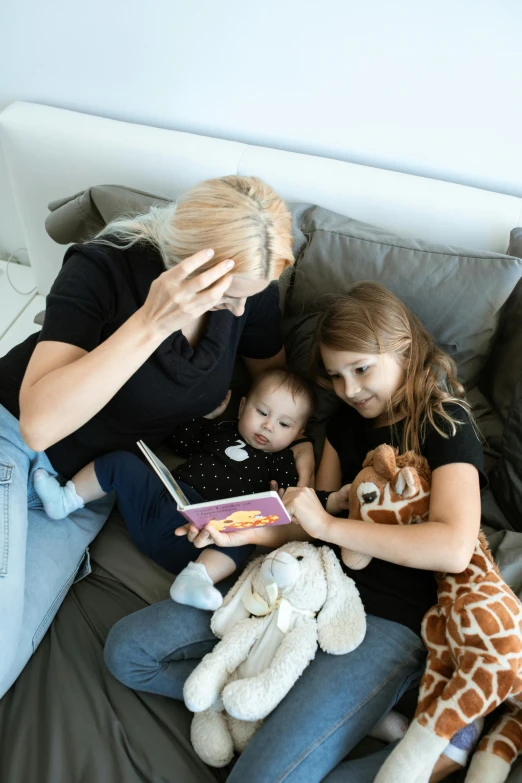 a woman sitting on a couch with two children and a stuffed giraffe, a cartoon, pexels contest winner, flatlay book collection, a blond, touching heads, gif