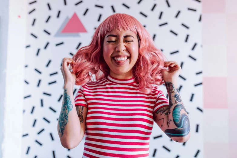 a woman with pink hair standing in front of a wall, trending on pexels, maximalism, earing a shirt laughing, wheres wally, geometric tattoos, cindy avelino