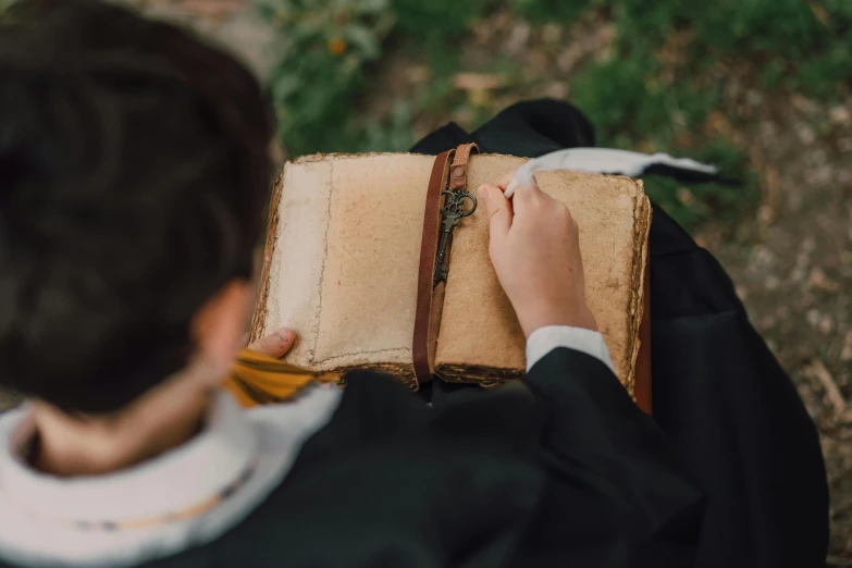 a close up of a person holding a book, by Emma Andijewska, pexels contest winner, renaissance, wearing robes and neckties, school class, field journal, birdseye view