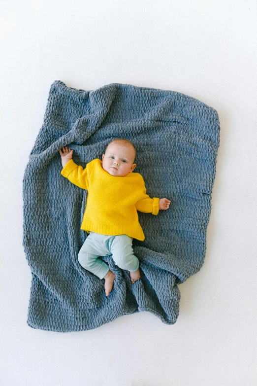 a baby laying on top of a blue blanket, trending on instagram, yellow and charcoal, full product shot, throw, small
