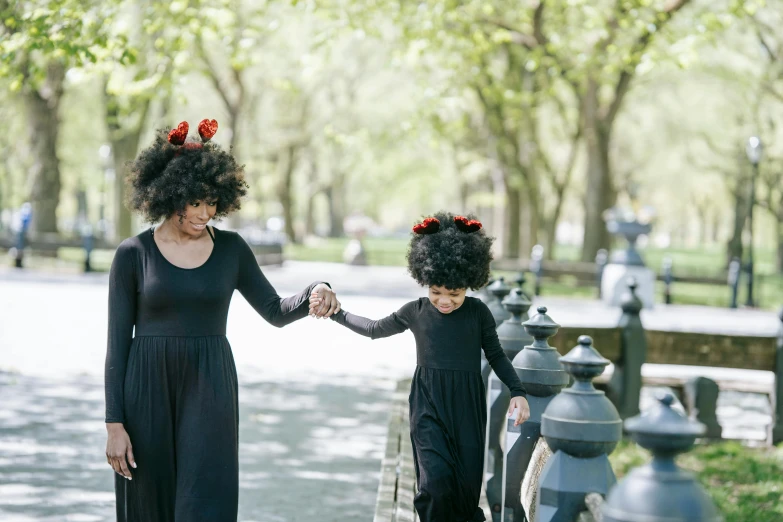 a woman and a child walking down a sidewalk, an album cover, pexels contest winner, black curly hair, central park, avacado halloween costumes, crimson - black beehive