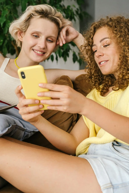 two women sitting on a couch looking at a cell phone, trending on pexels, wavy hair yellow theme, teenagers, promo image, bottom angle