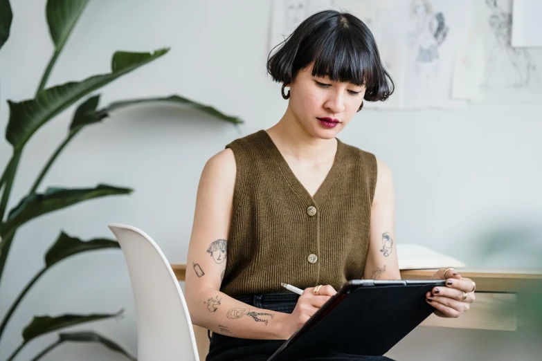 a woman sitting at a table writing on a clipboard, a cartoon, inspired by Ruth Jên, trending on pexels, of taiwanese girl with tattoos, female in office dress, portrait photo, slightly minimal