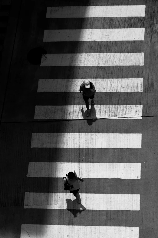 a couple of people that are walking across a street, a black and white photo, by Constantine Andreou, unsplash contest winner, postminimalism, back lit vertigo fear of heights, square lines, contre - jour, crosswalk