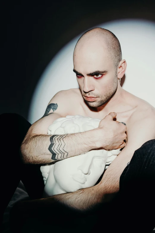 a bald man with tattoos sitting on a bed, an album cover, pexels contest winner, antipodeans, androgynous vampire, young greek man, dio brando, loving stare