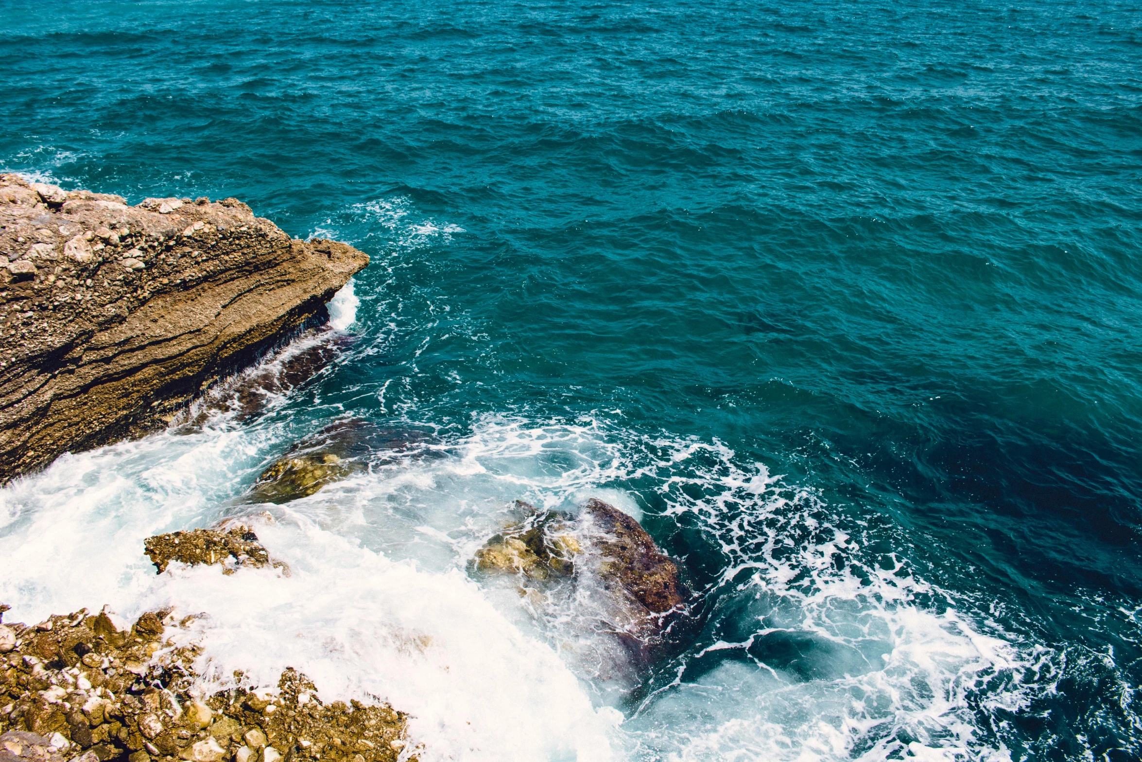 a large body of water next to a rocky shore, pexels contest winner, sea spray, looking down a cliff, manly, mediterranean