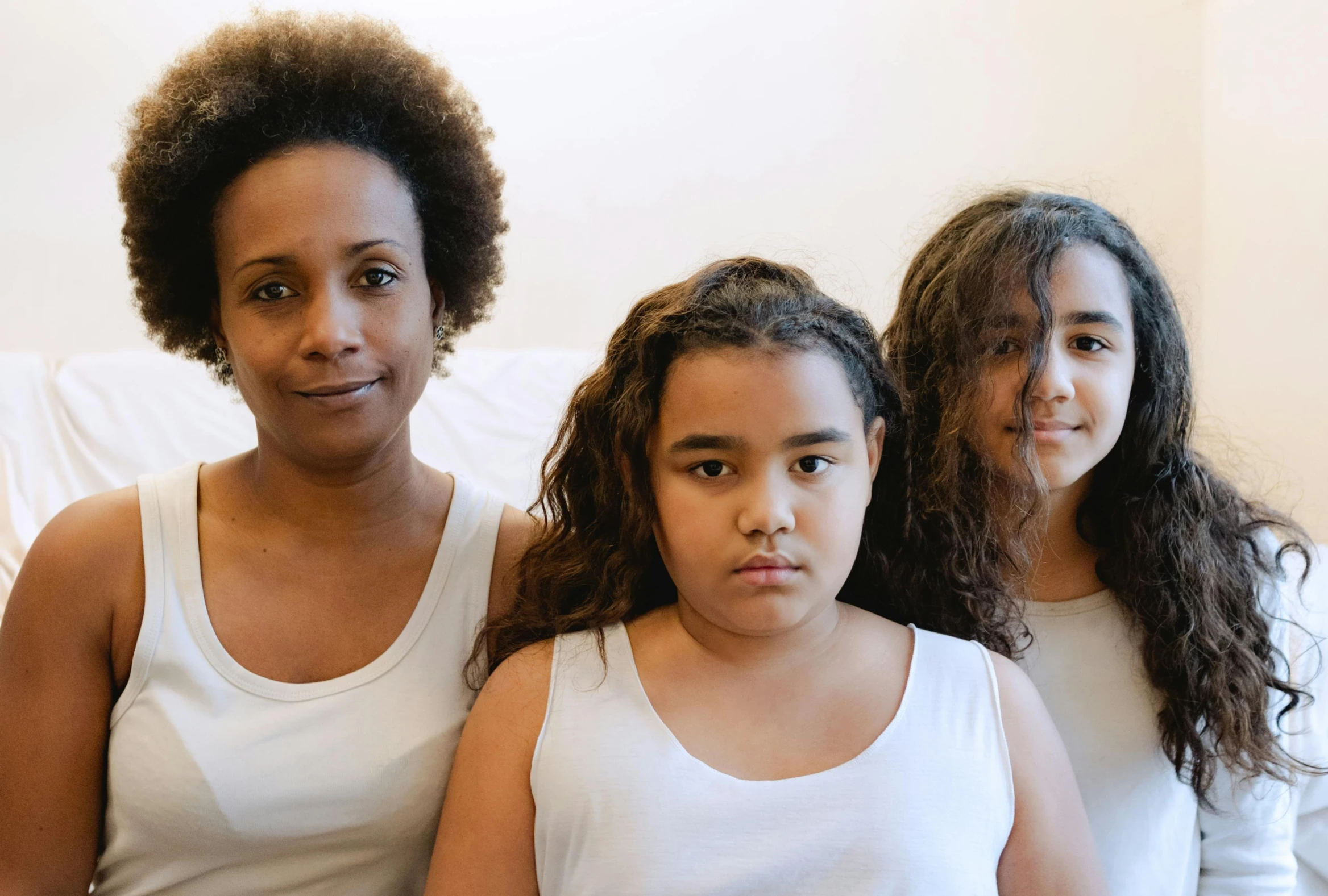 a group of women sitting on top of a bed, with textured hair and skin, family friendly, dressed in a white t shirt, medical image