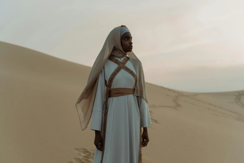 a woman standing in the middle of a desert, inspired by Osman Hamdi Bey, afrofuturism, billie eilish as a nun, diverse costumes, a medieval, cinematic. ”