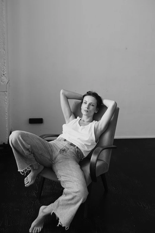 a black and white photo of a woman sitting in a chair, inspired by Peter Lindbergh, baggy jeans, evangeline lilly, dressed in a white t shirt, bella poarch