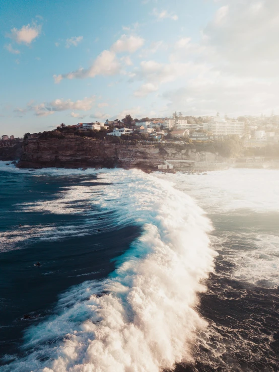 a person riding a surfboard on top of a wave, by Daniel Seghers, pexels contest winner, happening, bondi beach in the background, 4 k cinematic panoramic view, cliffside town, photo taken from a boat