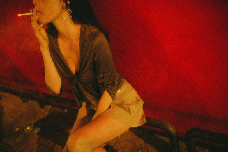 a woman sitting on a bench smoking a cigarette, an album cover, inspired by Nan Goldin, trending on pexels, renaissance, red wall, asian woman, in a nightclub, wearing red shorts