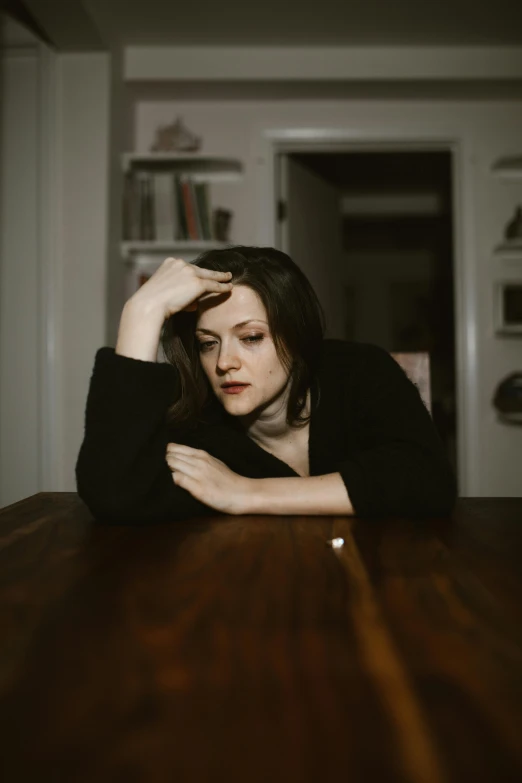 a woman sitting at a table with her head in her hands, inspired by Elsa Bleda, unsplash, renaissance, elisabeth moss, androgynous male, standing in a dimly lit room, low quality photo