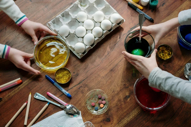 a group of people painting eggs on a table, trending on pexels, ingredients on the table, on a wooden desk, oil inks, thumbnail