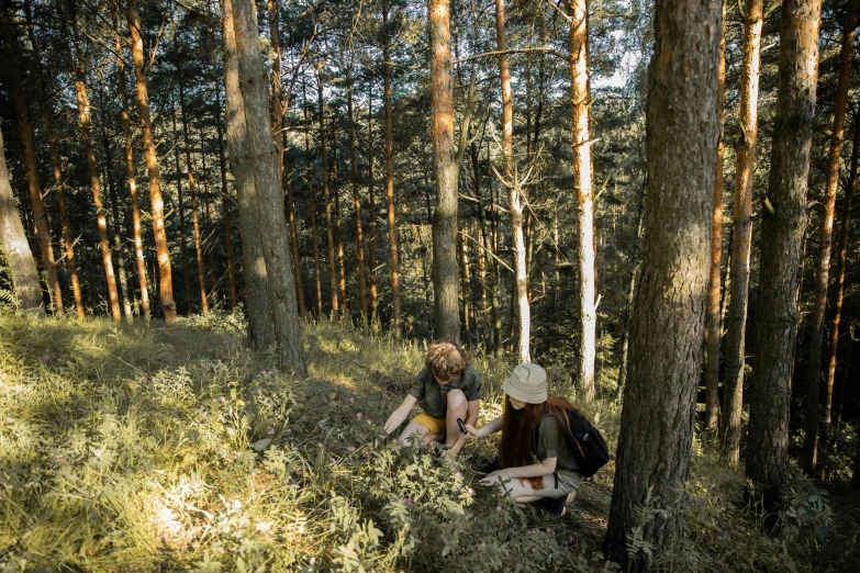 a couple of people that are sitting in the grass, by Emma Andijewska, pexels contest winner, trees and pines everywhere, humans exploring, avatar image, food. craft and adventure