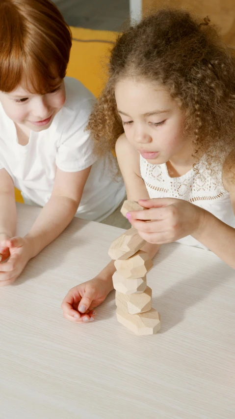 two children playing with wooden blocks on a table, inspired by Sarah Lucas, pexels contest winner, hexagonal shaped, light toned, videogame still, full product shot