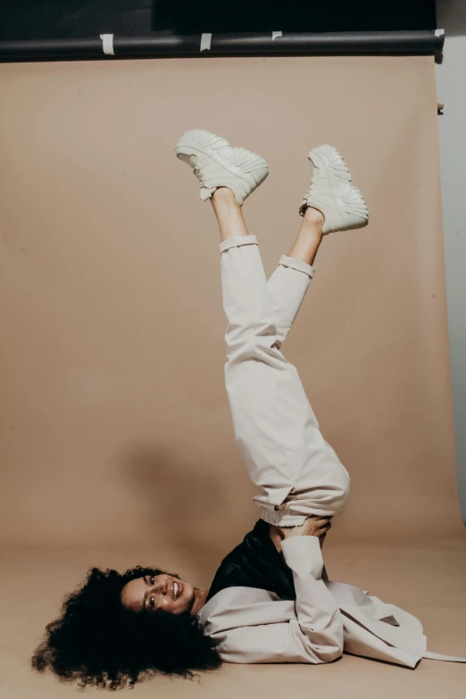 a woman doing a handstand in front of a backdrop, trending on pexels, sneaker photo, wearing off - white style, blank background, doing a sassy pose