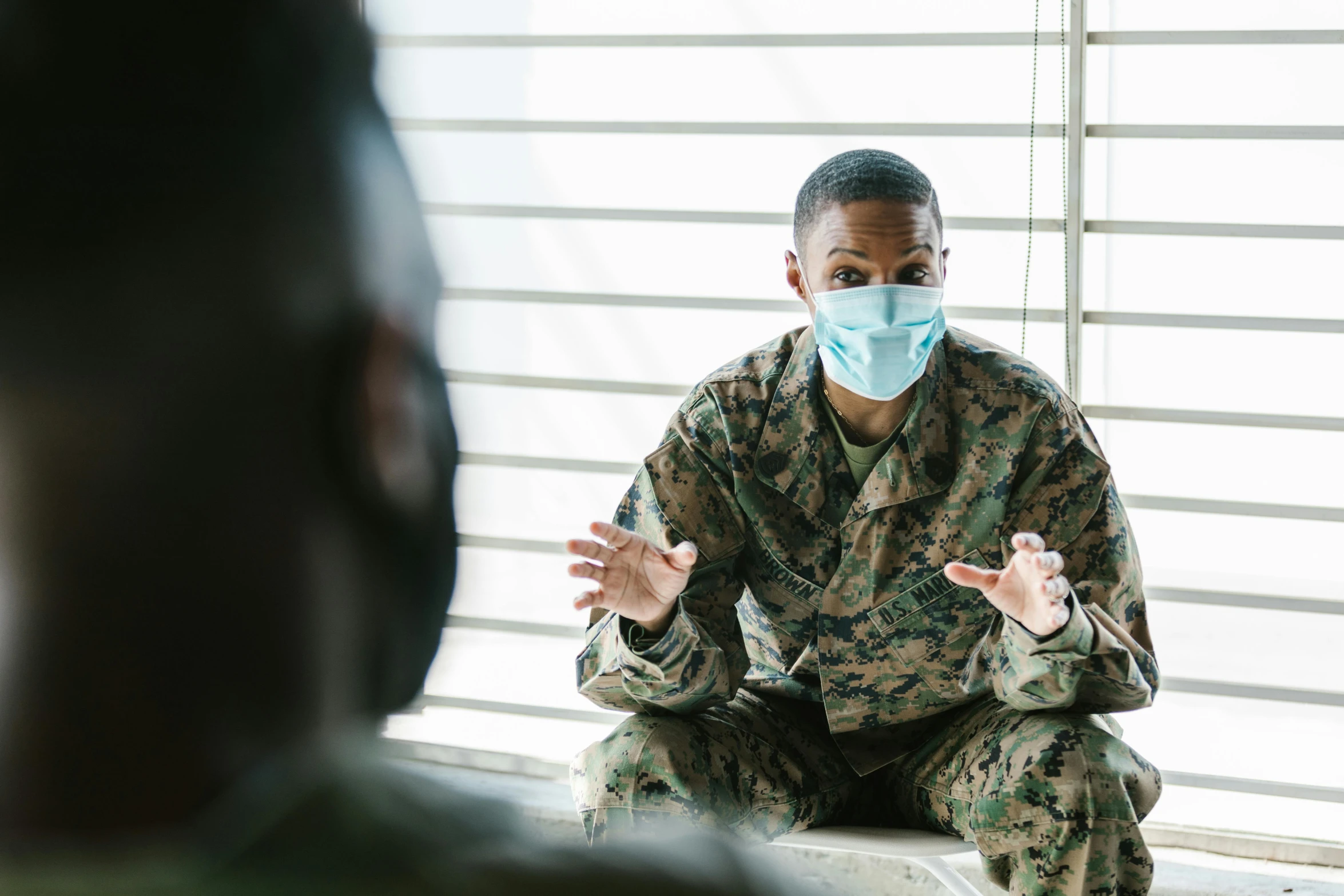 a man sitting in front of a window wearing a face mask, camouflage uniform, interview, marine, healthcare worker