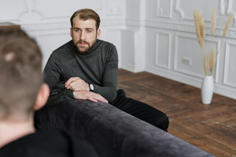 a man sitting on a couch in a living room, a photo, trending on pexels, renaissance, two buddies sitting in a room, wearing a black sweater, realistic professional photo, realistic »