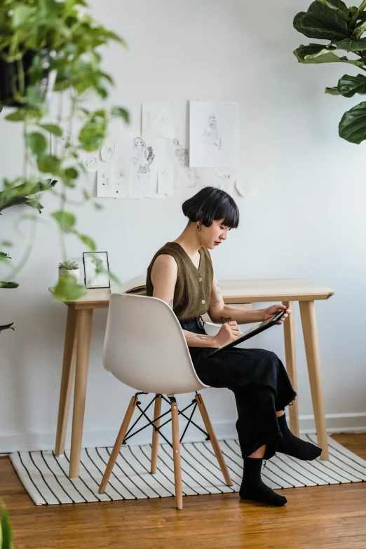 a woman sitting at a table using a tablet computer, pexels contest winner, process art, sitting on designer chair, plants, lulu chen, dwell