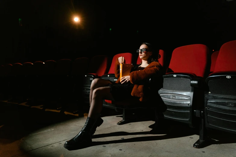 a woman sitting in a chair in a movie theater, inspired by Elsa Bleda, pexels contest winner, bauhaus, wearing 3 d glasses, sitting on a stone throne, in style of nan goldin, cinematic beer