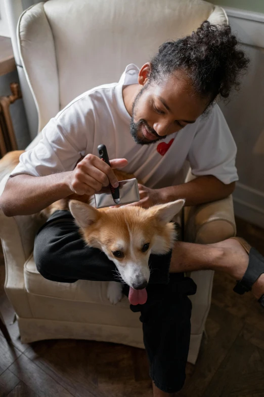 a man sitting in a chair petting a dog, by Julia Pishtar, hair detailing, jemal shabazz, corgi, carefully crafted
