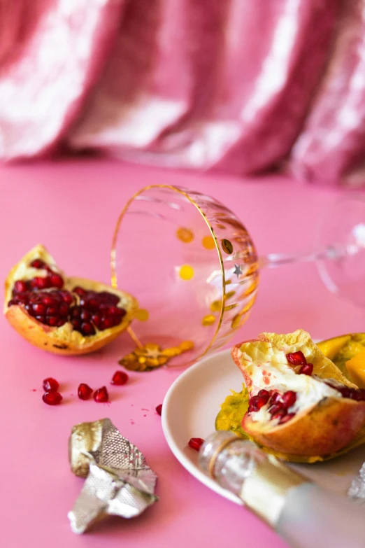 a white plate topped with pomegranate next to a glass of wine, a still life, by Sara Saftleven, trending on pexels, pop art, pink and gold color scheme, peeled oranges, sparkling crystals, bowl filled with food