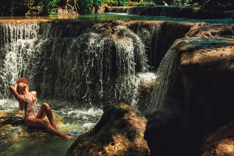 a woman sitting on a rock in front of a waterfall, an album cover, unsplash contest winner, sumatraism, paradise garden massage, loincloth, laos, thumbnail