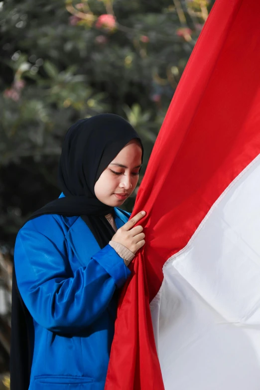 a woman in a blue jacket holding a red and white flag, unsplash, hurufiyya, jakarta, avatar image, panel, inauguration