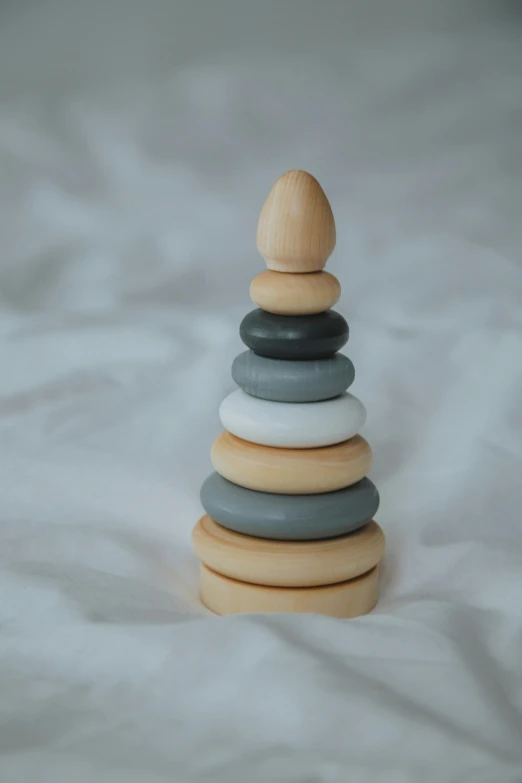 a stack of rocks sitting on top of a bed, by Eleanor Best, wooden art toys, halo / nimbus, grey backdrop, finger