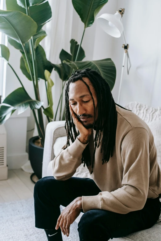 a man with dreadlocks sitting on a couch, trending on pexels, romanticism, she's sad, next to a plant, praying, someone sits in bed